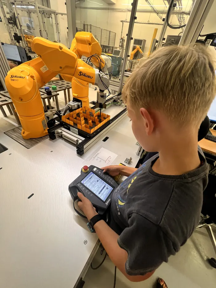 Účastník s ovládacím panelem u průmyslového robota.